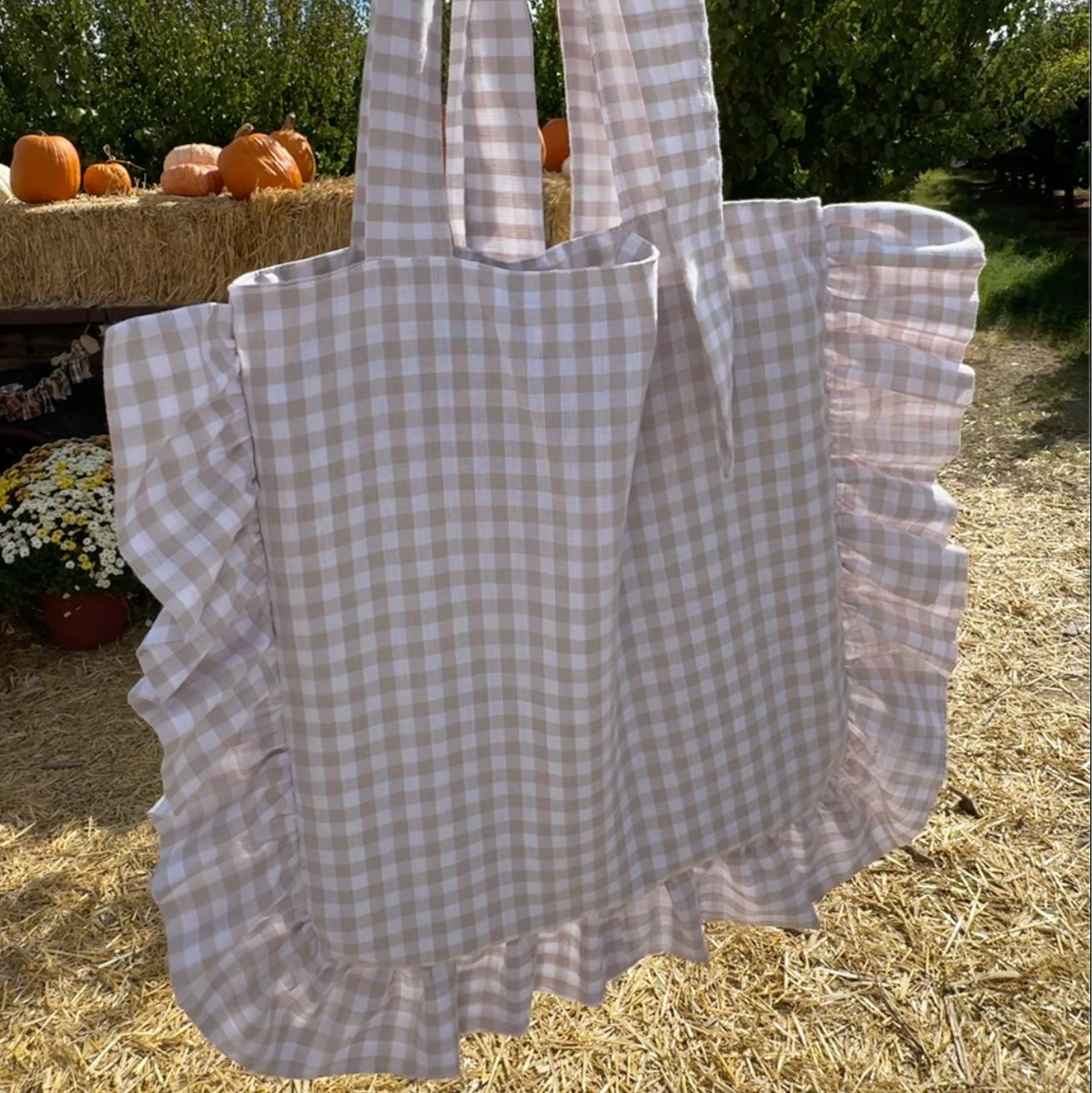 Checkered tote bag with ruffled edges held outdoors with trees and pumpkins in the background, bolsa tutorial bolsa con holanes y volantes.