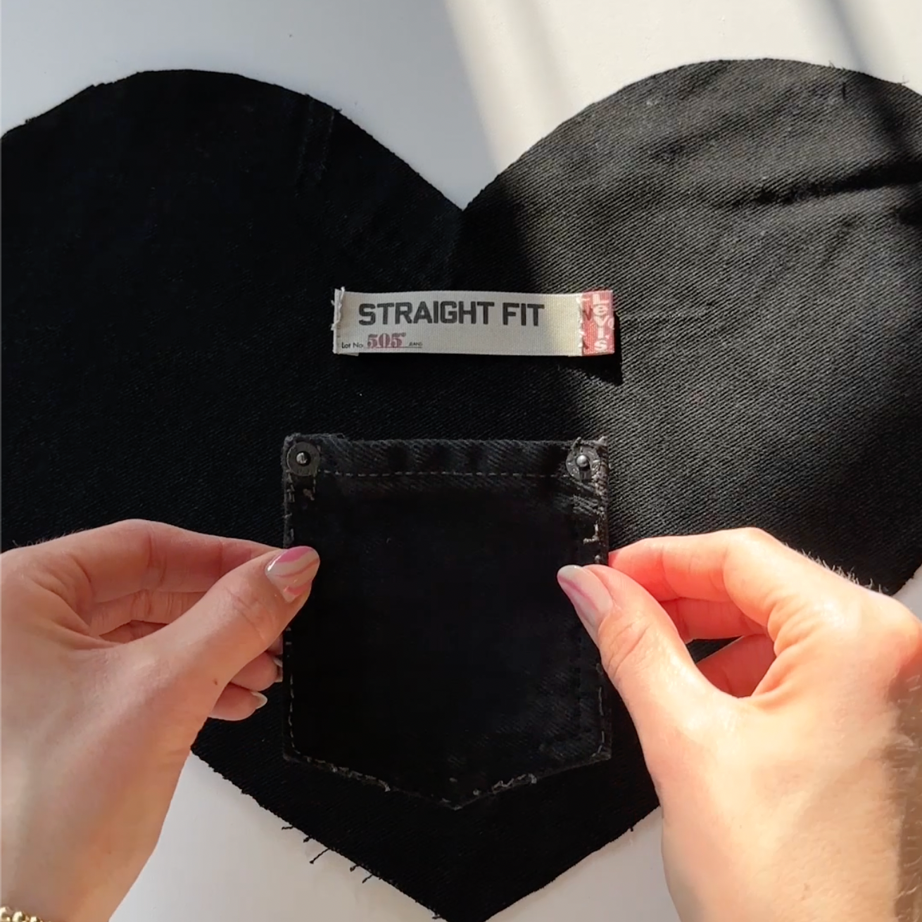 Black denim jeans with a 'Straight Fit' label held by hands against a white background