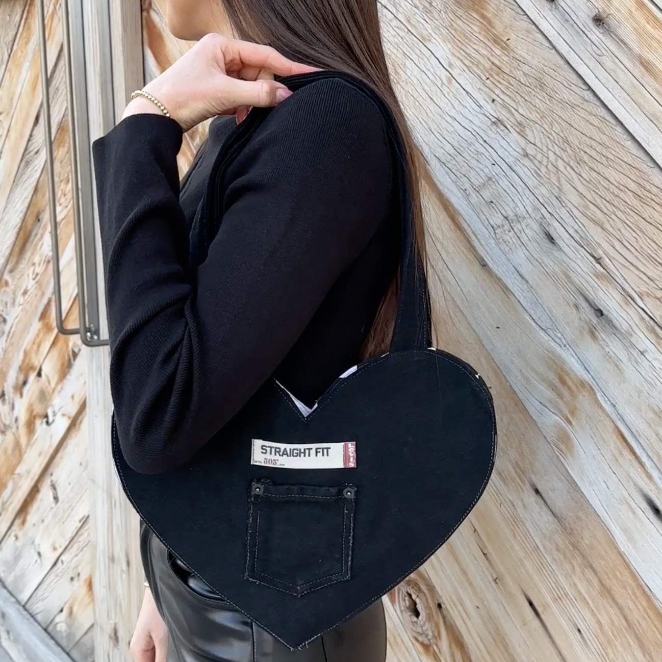 Person wearing a black jacket with a visible brand label heart tote bag against a wooden background