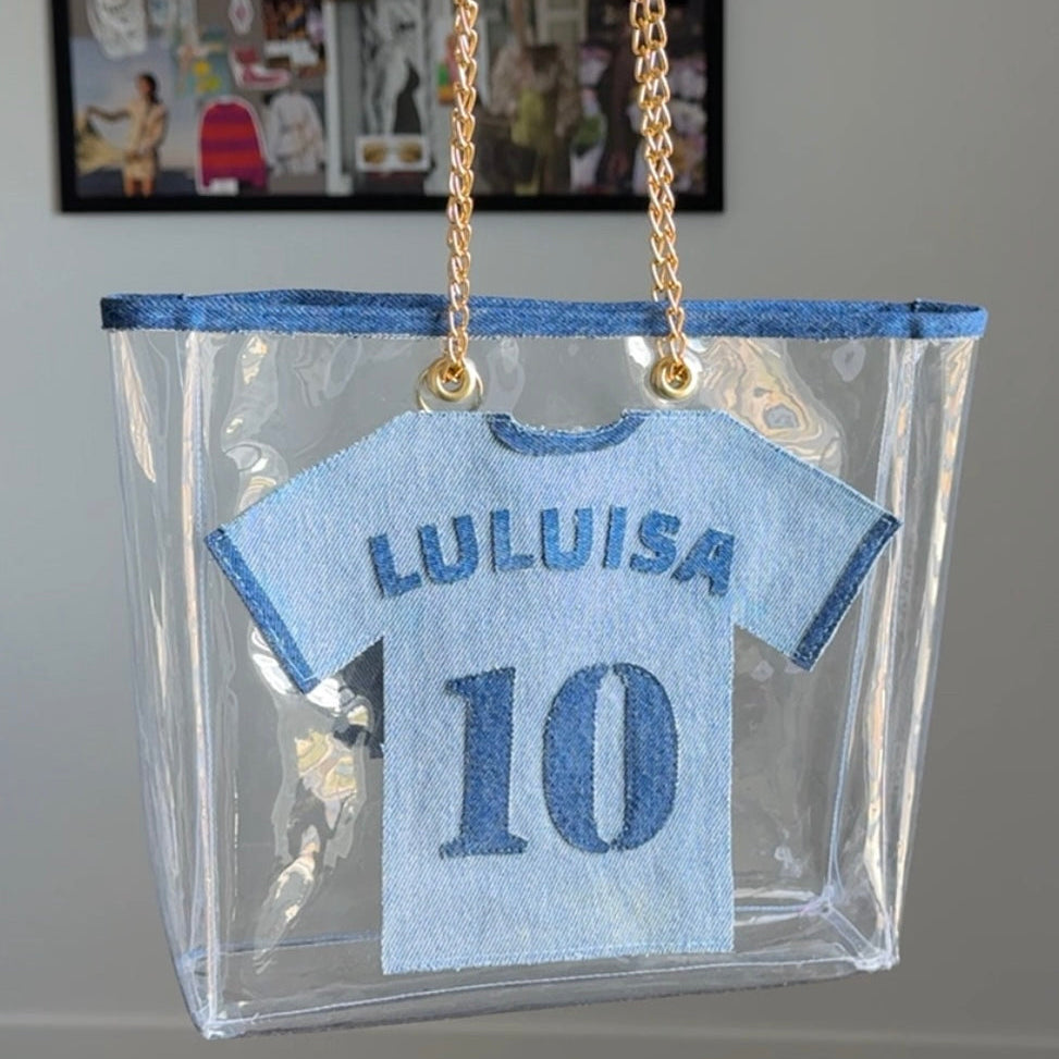 Clear bag with a blue shirt design featuring 'LULUISA' and number '10', held by a hand.